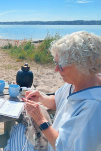 Frau strickt an einem Wollprojekt an einem Tisch am dänischen Wasser.